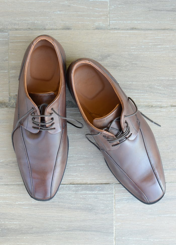 A pair of stylish brown leather dress shoes placed on a wooden floor, capturing modern fashion elegance.