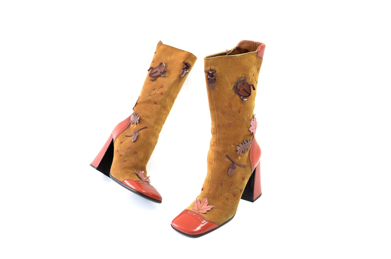 about-01 Pair of vintage suede brown boots with leather heels and nose decorated with tree leaves and bugs placed on white surface